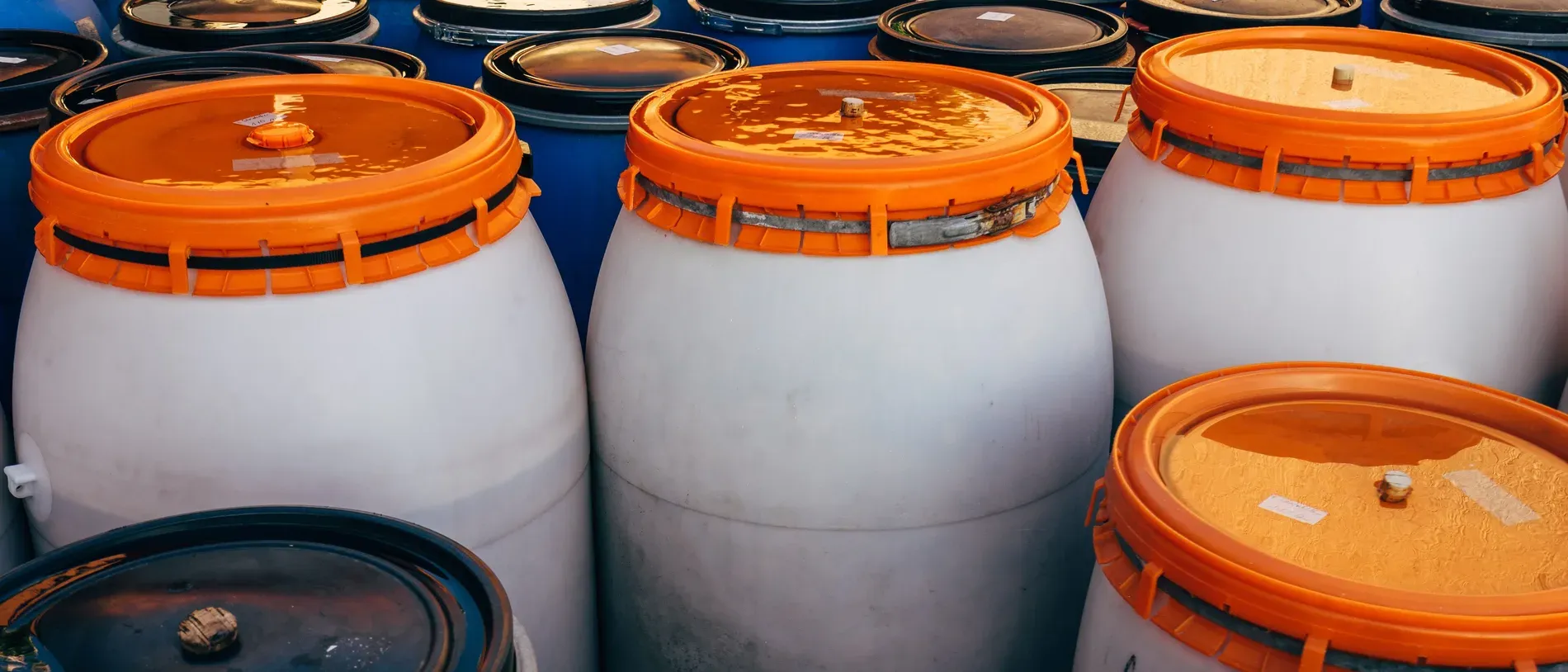 Bombonas plásticas de tampa laranja e tambores azuis empilhados num depósito